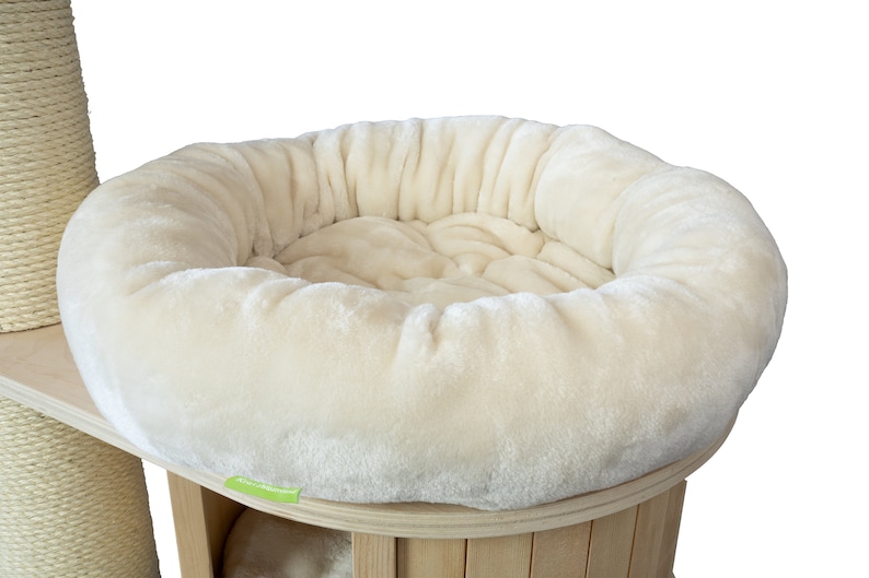 K&ouml;nnte beinhalten: Ein cremefarbenes Katzenbett mit einem weichen, runden Design. Das Bett ist Teil eines mehrst&ouml;ckigen Kratzbaums mit Holzsockel und einer mit Sisal umwickelten Kratzs&auml;ule. Die weiche Textur und die neutrale Farbe bieten einen gem&uuml;tlichen Platz f&uuml;r eine Katze.