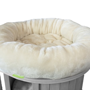 K&ouml;nnte beinhalten: Ein cremefarbenes, pl&uuml;schiges Haustierbett mit runder Form, das f&uuml;r Komfort konzipiert wurde. Das Bett ist Teil einer Katzenbaumstruktur, mit einem Holzsockel und einem Kratzbaum aus Sisal im Hintergrund.