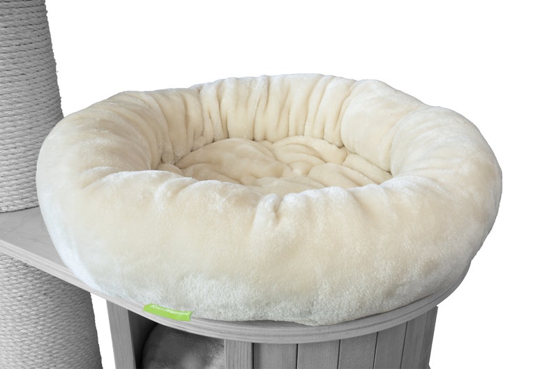 K&ouml;nnte beinhalten: Ein cremefarbenes, pl&uuml;schiges Haustierbett mit runder Form, das f&uuml;r Komfort konzipiert wurde. Das Bett ist Teil einer Katzenbaumstruktur, mit einem Holzsockel und einem Kratzbaum aus Sisal im Hintergrund.