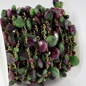 Può includere: Una bobina di catena in filo dorato con perline di rubino e zoisite sfaccettate in tonalità magenta intenso, verde bosco e nero. La catena è avvolta densamente, mostrando un motivo ripetitivo di maglie di filo e pietre con il testo SGJ.