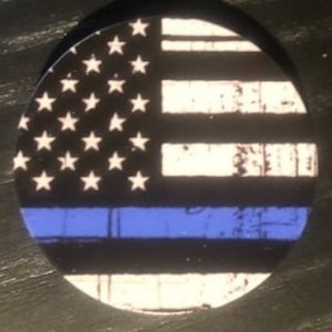 May include: A round phone grip with a distressed American flag design. The flag features a blue line across the bottom, representing support for law enforcement.