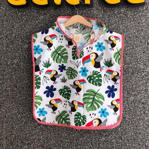 May include: White hooded towel with a red and white trim. The towel features a tropical print with toucans and green leaves.
