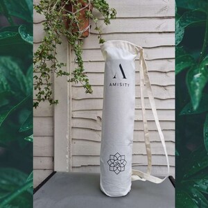 May include: White canvas yoga mat bag with a black strap and the word "AMISITY" printed on the front. The bag has a black and white lotus flower design.