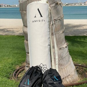 May include: Two black drawstring bags with the word "AMISITY" printed on them, and a white canvas bag with the word "AMISITY" printed on it. The bags are sitting on a green grassy surface.