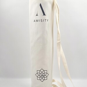 May include: A white canvas yoga mat bag with a black drawstring closure. The bag has a black logo that says "AMISITY" and a black lotus flower with an "OM" symbol in the center.