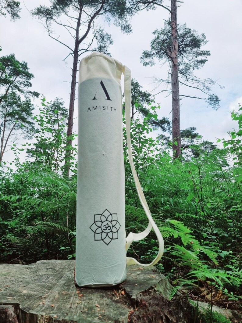 May include: A white yoga mat bag with a black logo that says "AMISITY" and a black and white Om symbol. The bag has a white strap.