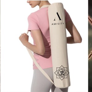 May include: A white yoga mat carrier with a black "A" logo and the word "AMISITY" printed on it. The carrier has a black Om symbol inside a flower design on the bottom.