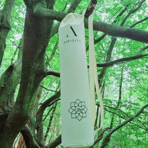May include: A white yoga mat bag with a black strap and the word "AMISITY" printed on the front. The bag has a black and white floral design with an "Om" symbol in the center.