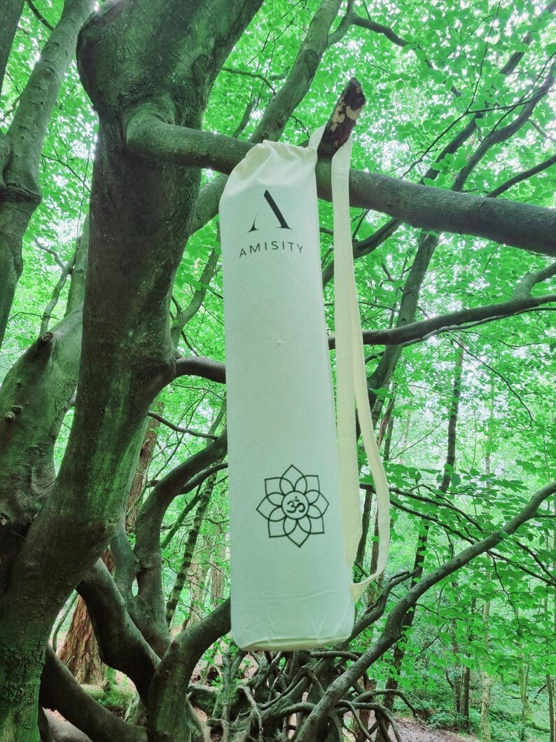 May include: A white yoga mat bag with a black strap and the word "AMISITY" printed on the front. The bag has a black and white floral design with an "Om" symbol in the center.