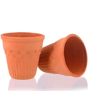 Puede incluir: Dos tazas de arcilla de color terracota. Las tazas tienen forma cónica con un borde ancho y una superficie texturizada. Una taza está en posición vertical, mientras que la otra está inclinada hacia un lado. Las tazas probablemente son para servir bebidas.