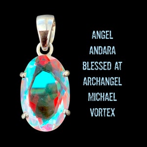 Puede incluir: Un colgante de plata con un gran cristal de Andara de forma ovalada con reflejos azules, verdes y rojos iridiscentes. El texto "ANGEL ANDARA BLESSED AT ARCHANGEL MICHAEL VORTEX" está escrito en azul sobre un fondo negro.