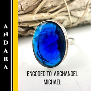 Puede incluir: Un anillo de plata con una piedra preciosa grande, ovalada y azul oscuro. El anillo está sobre salvia blanca y una superficie blanca. El texto de la imagen dice "ANDARA" y "ENCODED TO ARCHANGEL MICHAEL."