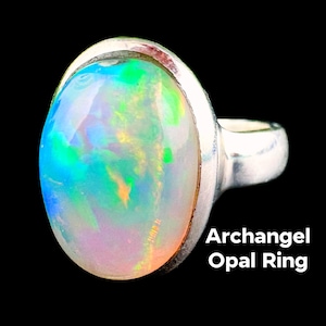 Puede incluir: Un anillo de plata con una gran piedra de ópalo ovalada. El ópalo muestra un vibrante juego de colores, con tonos de azul, verde y naranja. El texto "Archangel Opal Ring" se muestra en blanco.