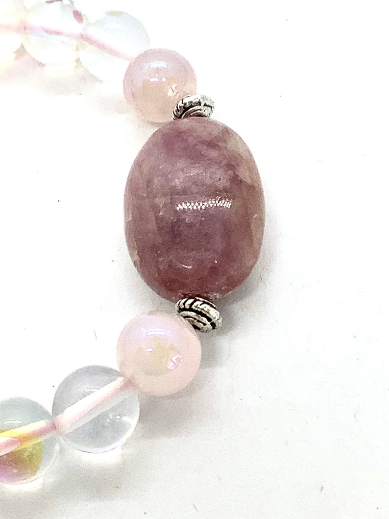May include: A pink and clear crystal bracelet with silver accents. The bracelet features a large oval-shaped pink crystal bead.