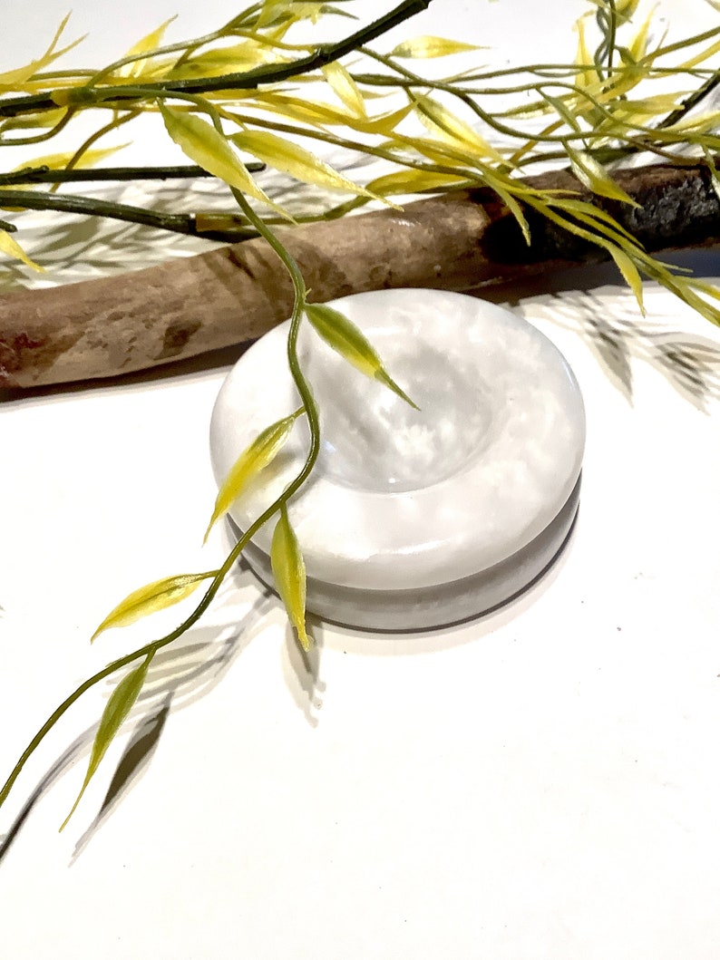 Pu&ograve; includere: Un piatto rotondo in marmo bianco con un centro leggermente incavato. Il piatto &egrave; composto da due pezzi, uno impilato sull'altro. Il piatto &egrave; su una superficie bianca.