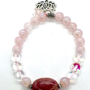 May include: A pink and clear crystal bracelet with a silver lotus charm. The bracelet features round beads and a larger oval-shaped bead.