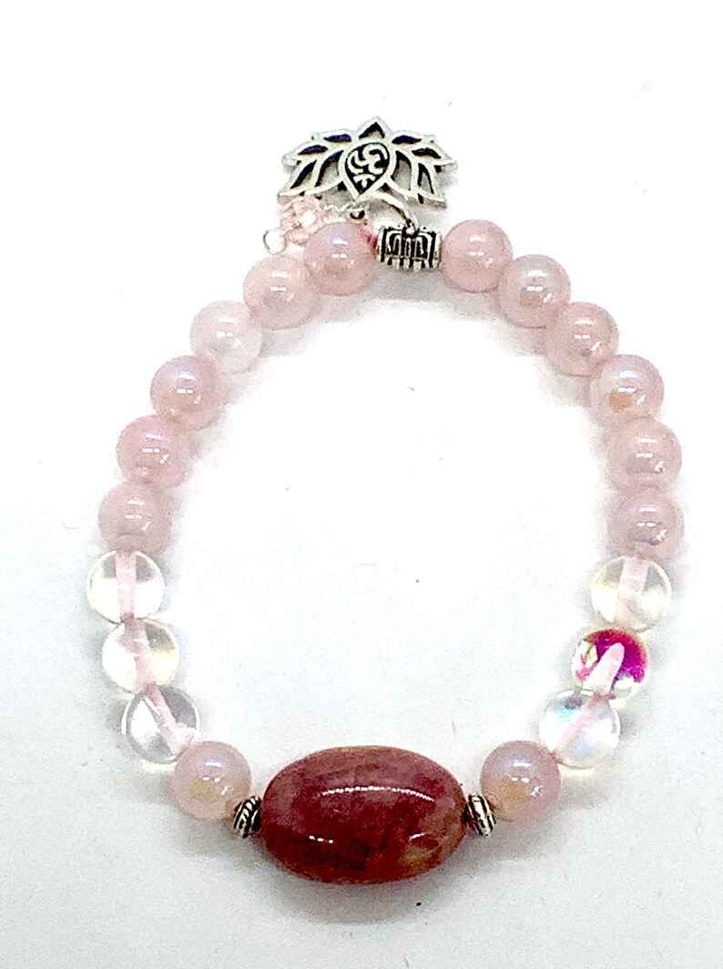May include: A pink and clear crystal bracelet with a silver lotus charm. The bracelet features round beads and a larger oval-shaped bead.