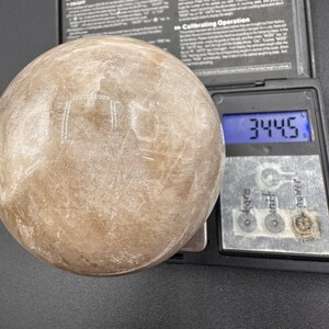 Pode incluir: Uma grande esfera branca transl&uacute;cida com uma superf&iacute;cie lisa. A esfera est&aacute; sendo pesada em uma balan&ccedil;a digital que mostra 344,5 gramas.