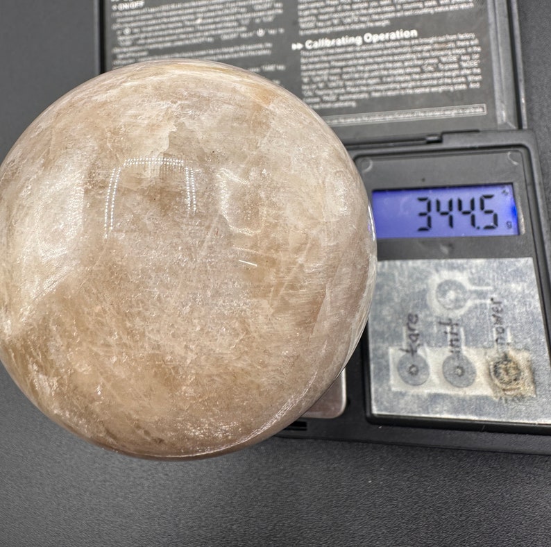 Pode incluir: Uma grande esfera branca transl&uacute;cida com uma superf&iacute;cie lisa. A esfera est&aacute; sendo pesada em uma balan&ccedil;a digital que mostra 344,5 gramas.