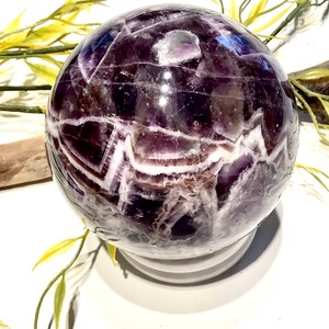 Pu&ograve; includere: Una grande sfera di ametista con un motivo a spirale di viola e bianco. La sfera &egrave; lucidata e ha una finitura lucida.