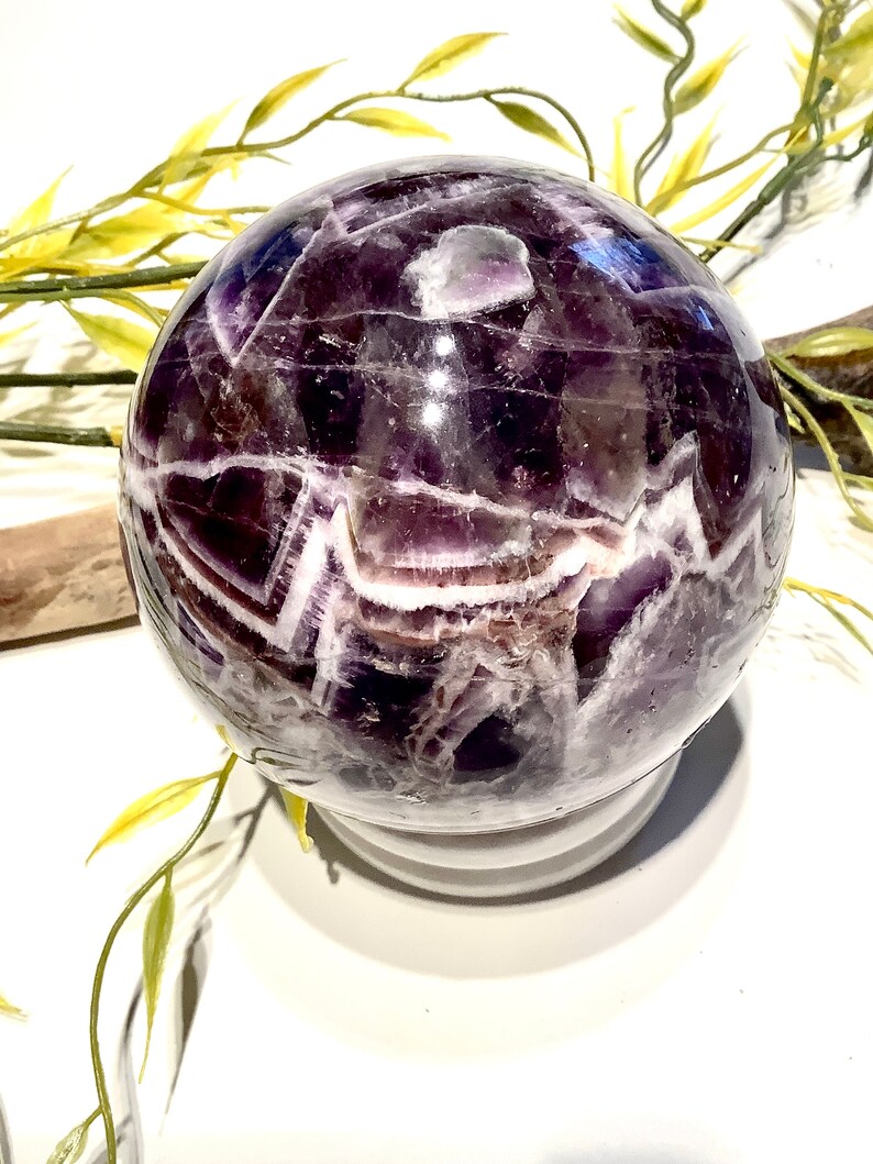 Pu&ograve; includere: Una grande sfera di ametista con un motivo a spirale di viola e bianco. La sfera &egrave; lucidata e ha una finitura lucida.