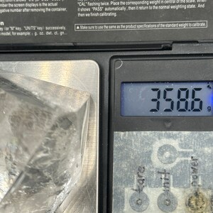 May include: A digital scale displays 358.6 grams. The scale has a silver weighing surface with control buttons labeled "tare", "unit", and "power". A clear plastic bag is partially visible on the scale.