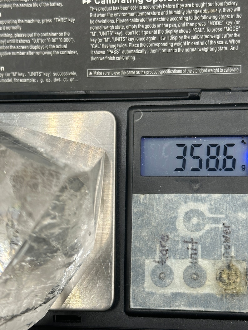 May include: A digital scale displays 358.6 grams. The scale has a silver weighing surface with control buttons labeled "tare", "unit", and "power". A clear plastic bag is partially visible on the scale.