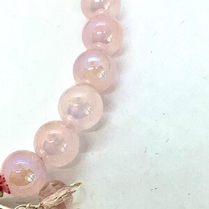 May include: A pink beaded bracelet with a silver charm. The beads are iridescent and have a slight shimmer.