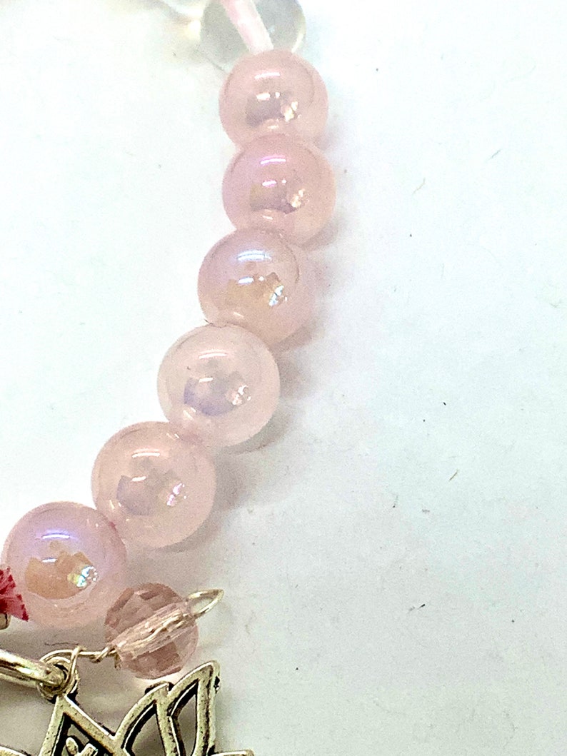 May include: A pink beaded bracelet with a silver charm. The beads are iridescent and have a slight shimmer.