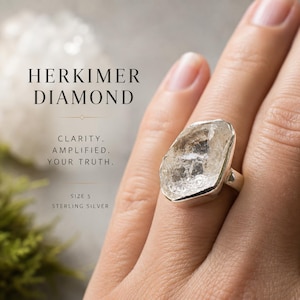 Peut inclure: Une bague en argent sterling avec une pierre précieuse Herkimer diamond brute et transparente. Le texte sur l'image indique : HERKIMER DIAMOND, CLARITY. AMPLIFIED. YOUR TRUTH., SIZE 5, STERLING SILVER. La bague possède un anneau en métal poli.