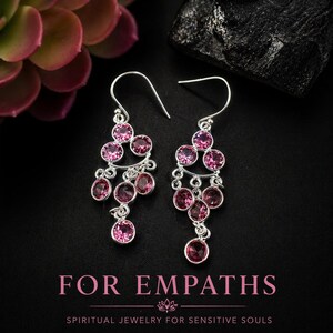 May include: Silver earrings featuring multiple pink gemstones in a chandelier design. The earrings are set against a black background with the text "FOR EMPATHS" and "SPIRITUAL JEWELRY FOR SENSITIVE SOULS".