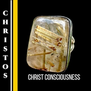 May include: A rectangular ring with a clear, textured stone containing golden, needle-like inclusions. The ring has a silver band. The words "CHRIST CONSCIOUSNESS" are printed in white on a black background.