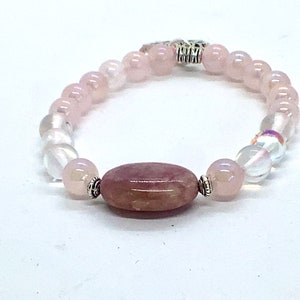 May include: A pink and white beaded bracelet with a larger oval-shaped pink stone in the center. The bracelet has a silver clasp.