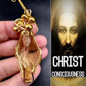 Puede incluir: Un colgante dorado con un cristal en forma de lágrima, envuelto en alambre. El colgante cuelga de una fina cadena dorada. La imagen también incluye un retrato de Jesús con las palabras "CHRIST CONSCIOUSNESS".