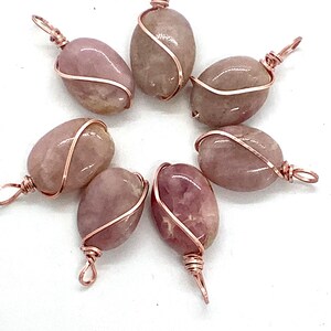 May include: Seven pink and white oval-shaped stones wrapped in copper wire with a loop at the top for hanging.