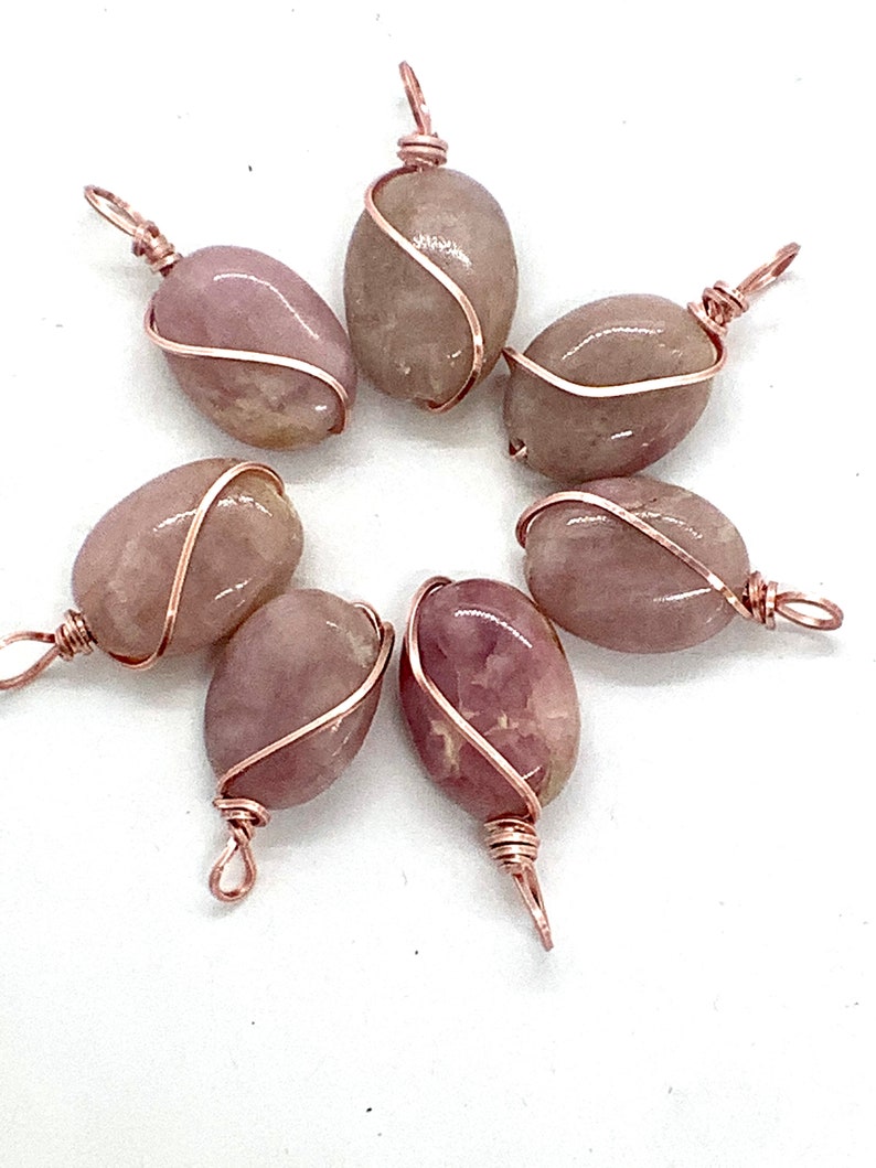 May include: Seven pink and white oval-shaped stones wrapped in copper wire with a loop at the top for hanging.