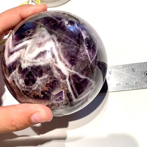Pu&ograve; includere: Una grande sfera di ametista viola con inclusioni bianche e marroni. La sfera ha un diametro di circa 5 cm.