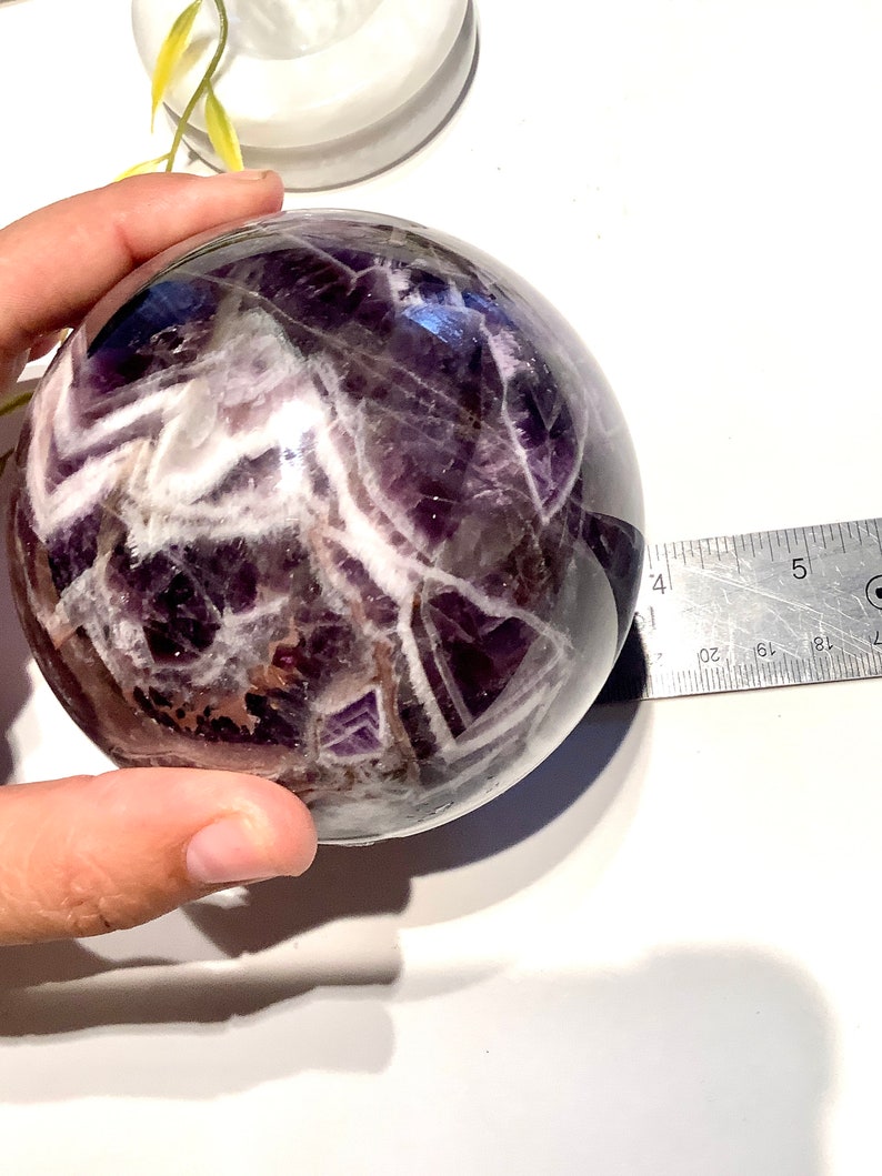 Pu&ograve; includere: Una grande sfera di ametista viola con inclusioni bianche e marroni. La sfera ha un diametro di circa 5 cm.