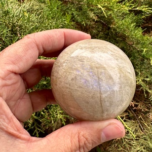 Pode incluir: Uma esfera lisa de cristal de selenite, de cor branca e cinza. A esfera est&aacute; sendo segurada em uma m&atilde;o.