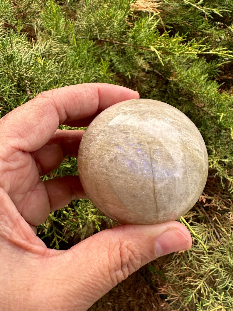 Pode incluir: Uma esfera lisa de cristal de selenite, de cor branca e cinza. A esfera est&aacute; sendo segurada em uma m&atilde;o.