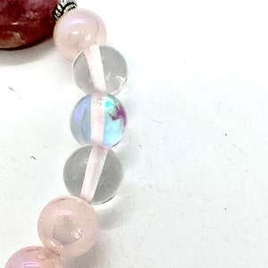 May include: A pink and clear crystal bracelet with a silver clasp. The bracelet features round beads of various sizes and a larger, oval-shaped bead.