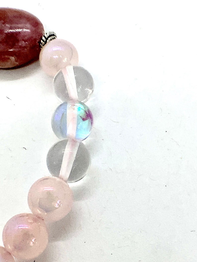 May include: A pink and clear crystal bracelet with a silver clasp. The bracelet features round beads of various sizes and a larger, oval-shaped bead.