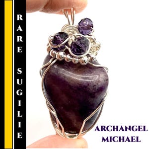 May include: A heart-shaped purple sugilite pendant wrapped in silver wire. The pendant is adorned with three purple crystal accents and the words "Archangel Michael". The left side of the image has the word "Rare Sugilite".