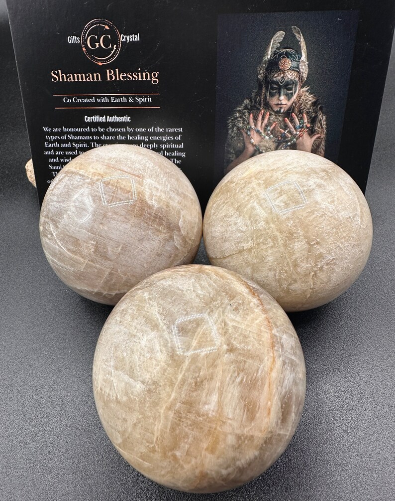 Pode incluir: Tr&ecirc;s esferas de selenita bege com uma textura cristalina branca. As esferas est&atilde;o dispostas em uma forma&ccedil;&atilde;o triangular sobre uma superf&iacute;cie cinza escura. O texto "Shaman Blessing" &eacute; vis&iacute;vel no fundo.