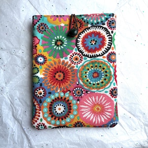 May include: A rectangular fabric sleeve featuring a vibrant, multi-colored floral pattern with circular motifs in shades of pink, orange, yellow, green, and blue. The top edge includes a black elastic cord with a small black plastic toggle closure.