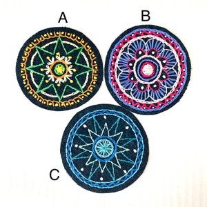 May include: Three round, embroidered patches with intricate designs. Patch A features a starburst pattern in green, orange, and yellow on a navy blue background. Patch B has a floral design in pink, white, and blue. Patch C has a blue star design.
