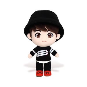 May include: A plush doll of a person wearing a black bucket hat, black and white striped long-sleeve shirt, black pants, and red shoes. The doll has brown hair and large brown eyes. The doll is standing upright.