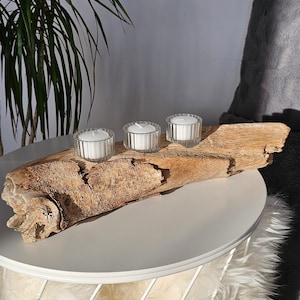 Peut inclure: Trois bougies blanches dans des bougeoirs en verre sont disposées sur une branche de bois flotté, qui est placée sur une table blanche avec une base en fourrure blanche.