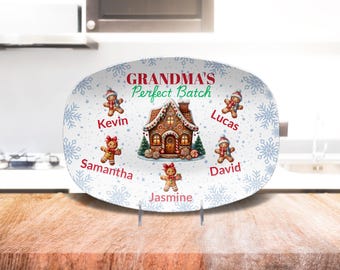 Könnte beinhalten: Weiße ovale Servierplatte mit einem Lebkuchenhaus und Lebkuchenmännern. Die Platte hat ein blaues und weißes Schneeflockenmuster und den Text "Grandma's Perfect Batch". Die Lebkuchenmänner sind mit den Namen Kevin, Samantha, Jasmine, Lucas und David beschriftet.