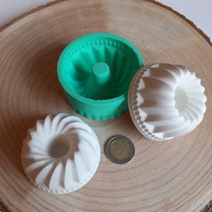 Könnte beinhalten: Drei Silikonformen zum Backen, zwei sind weiß und eine ist grün. Die Formen sind wie ein Bundkuchen mit einem geriffelten Design geformt. Die Formen befinden sich auf einer Holzoberfläche.